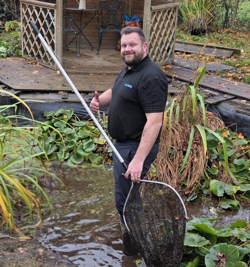 Technician carrying out a deep pond clean with professional equipment near a garden pond